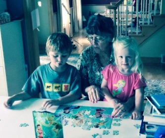 A woman and two small children working a jigsaw puzzle at a table by a window