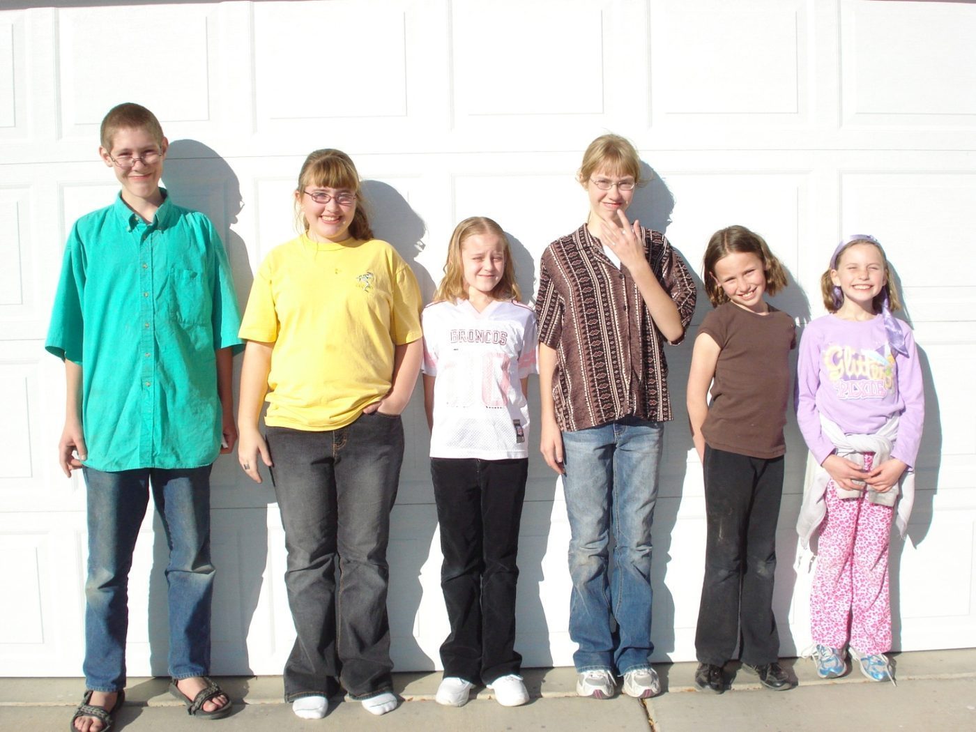 Six children lined up against a white garage door