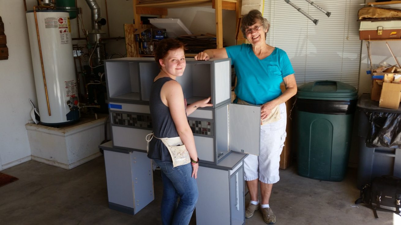 Two women beside a white-and-grey bed unit in the garage workshop