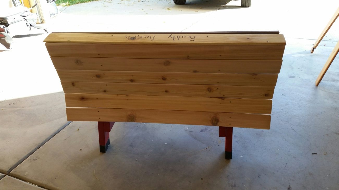 The buddy bench folded flat into its table form, red legs, on the garage floor