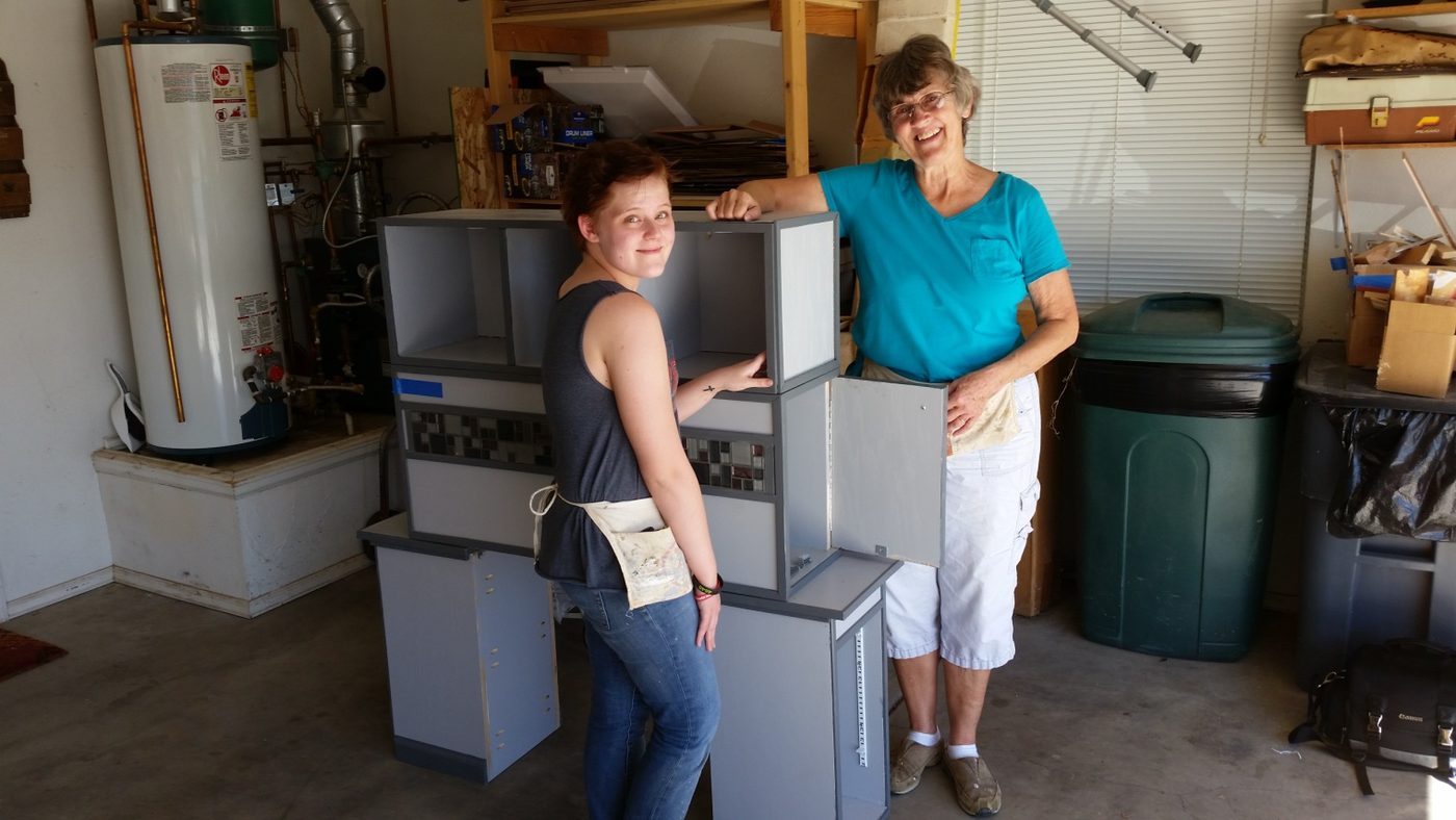 Two people in the garage beside the part-built white-and-grey twin bed unit